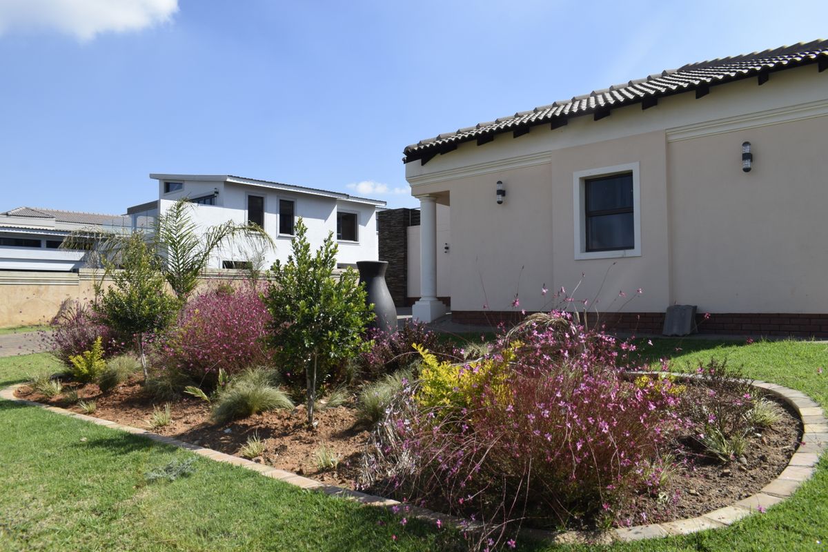 A well-maintained rear garden featuring landscaped flower beds with brick edging, adjacent to the side elevation of the house with exterior wall lighting.