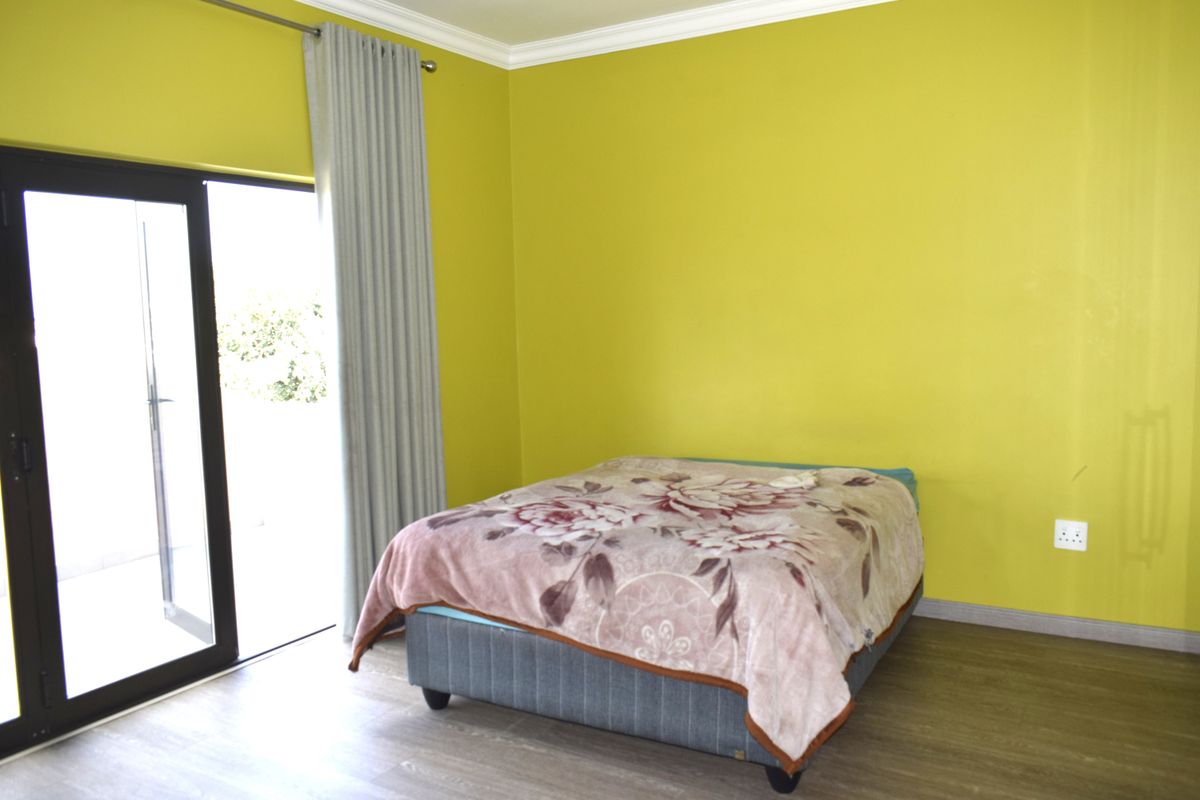 A bedroom featuring laminate flooring, bright yellow walls, and a sliding glass door providing access to the exterior.