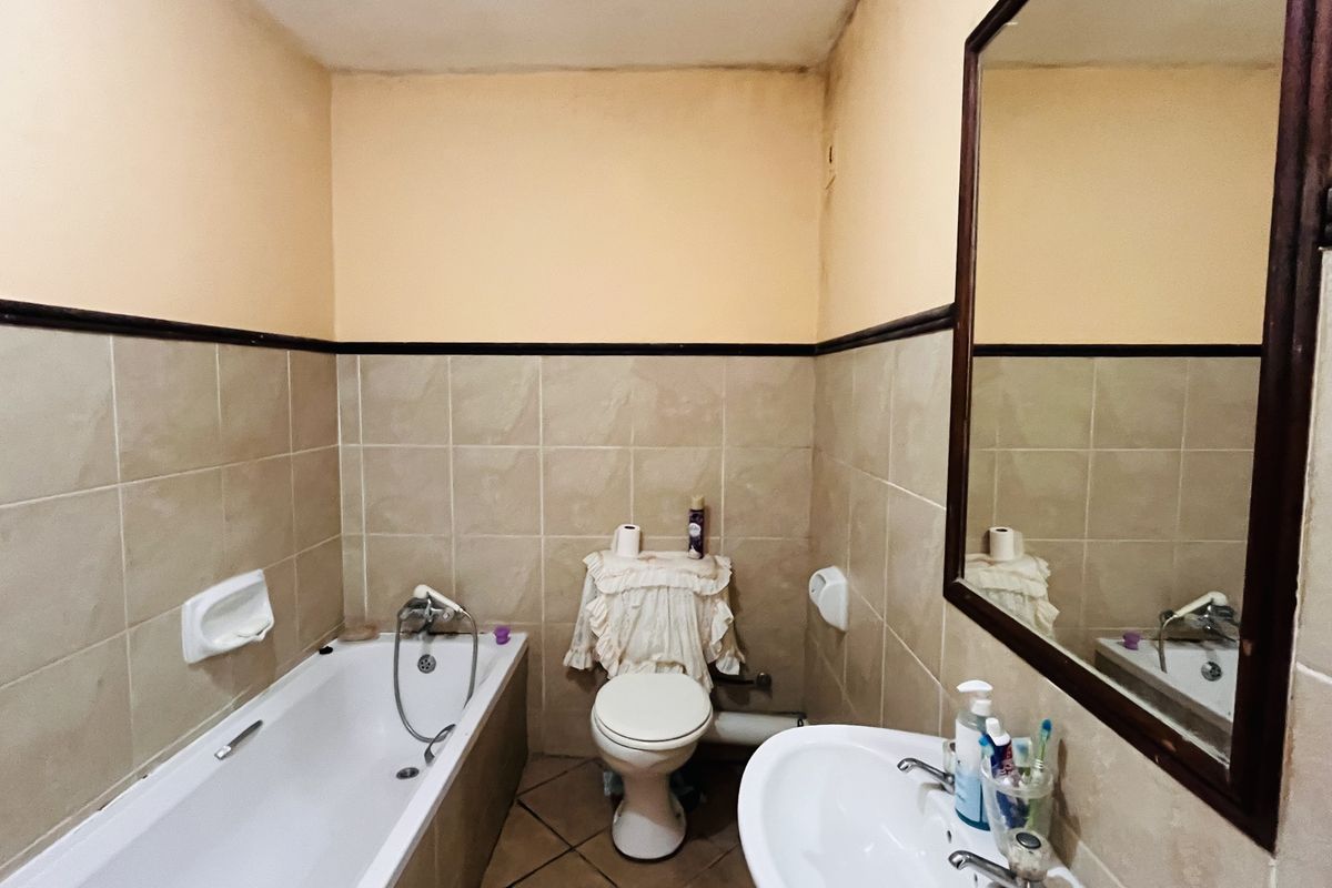 A dated bathroom featuring a standard bathtub, pedestal basin, and wall-mounted mirror with neutral ceramic tiling and painted walls.