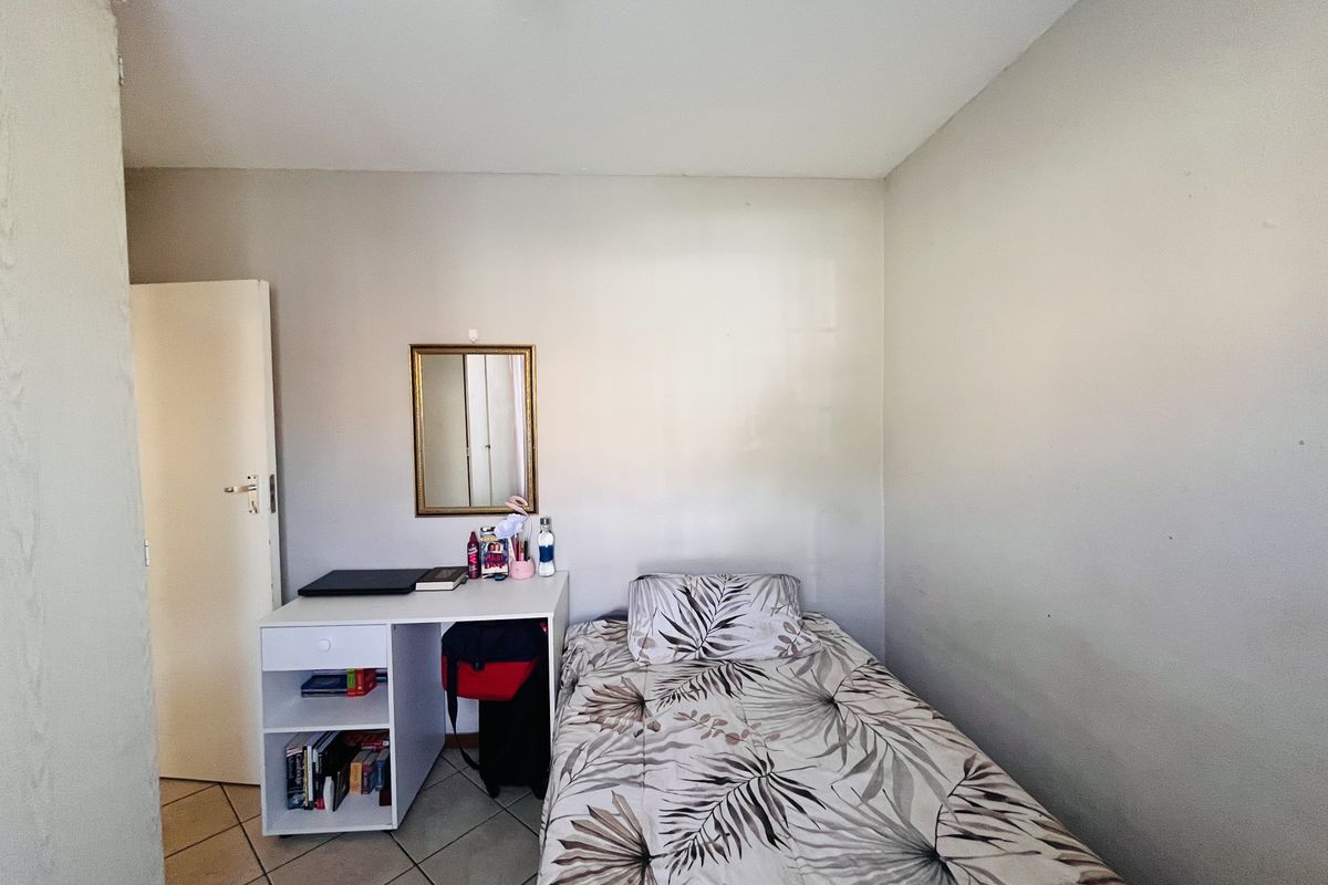 A compact bedroom featuring tiled flooring and neutral wall finishes, providing a functional space for a single bed and study area.