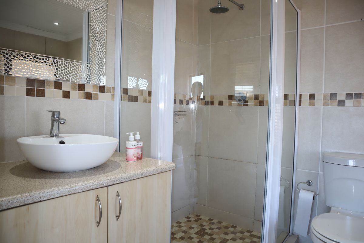 A functional bathroom featuring a vessel sink vanity, a glass-enclosed shower, and neutral wall tiling with decorative mosaic accents.