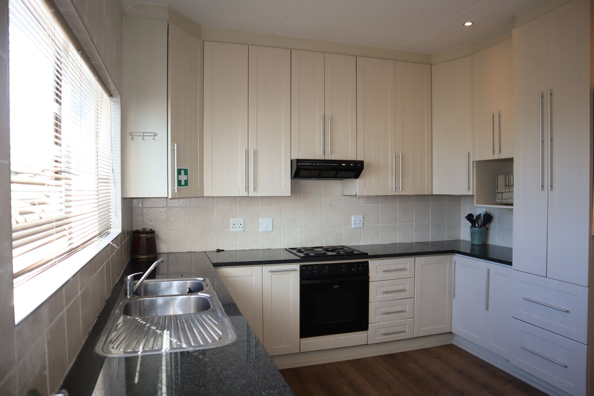 A clean, functional kitchen featuring neutral cabinetry, granite countertops, a built-in oven, electric hob, and a double bowl sink with a tiled backsplash.