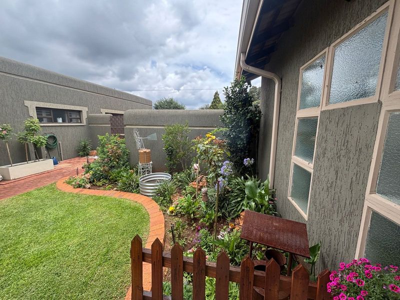 A well-maintained rear garden area featuring a brick-paved pathway, landscaped garden beds, and a secure boundary wall with integrated guttering.
