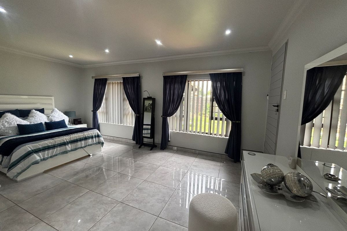 Spacious bedroom featuring large format floor tiles, recessed downlighting, and dual windows with vertical blinds, offering a clean and well-maintained living space.
