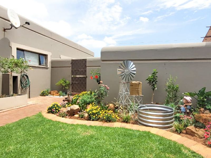 A well-maintained private garden featuring a manicured lawn, paved pathways, and established landscaped flower beds enclosed by a solid boundary wall.