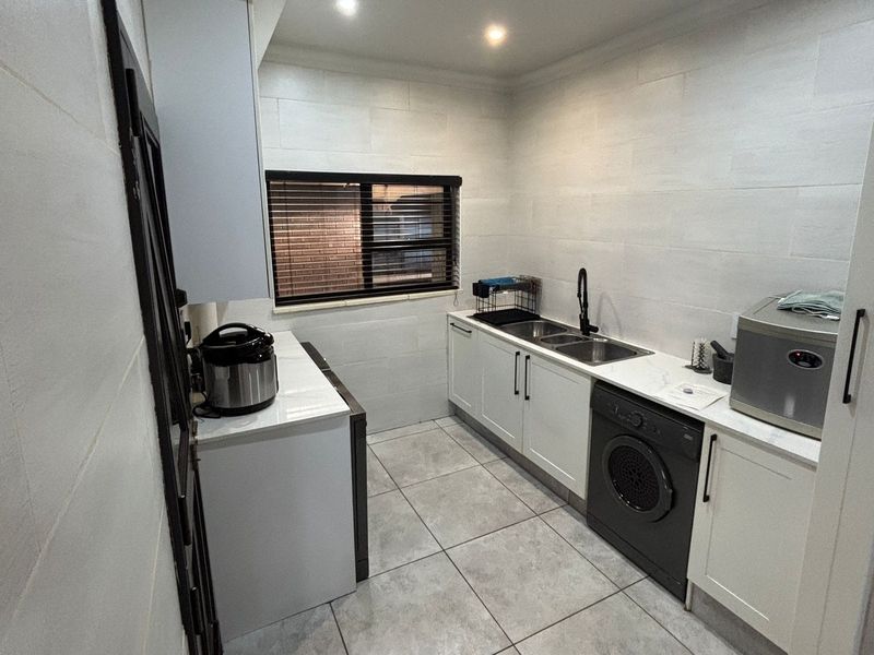 A functional laundry room featuring white built-in cabinetry, a double basin sink, tiled walls, and tiled flooring with recessed lighting.