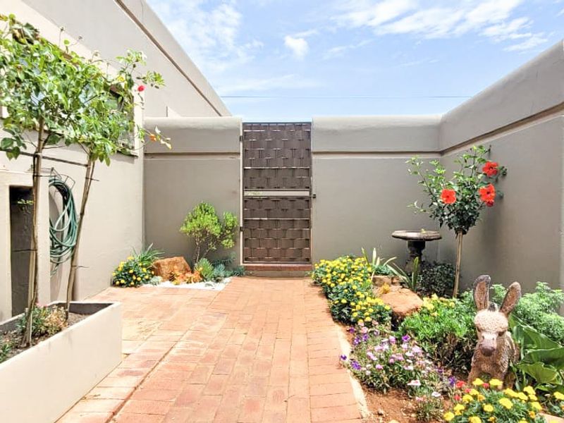 A well-maintained rear courtyard featuring brick paving, a secure metal gate, and established garden beds with built-in planters.