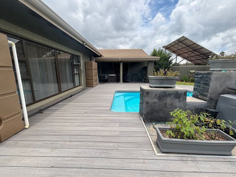 Outdoor pool area featuring modern composite decking, a stone-clad water feature, and a covered patio space with access to the main house.