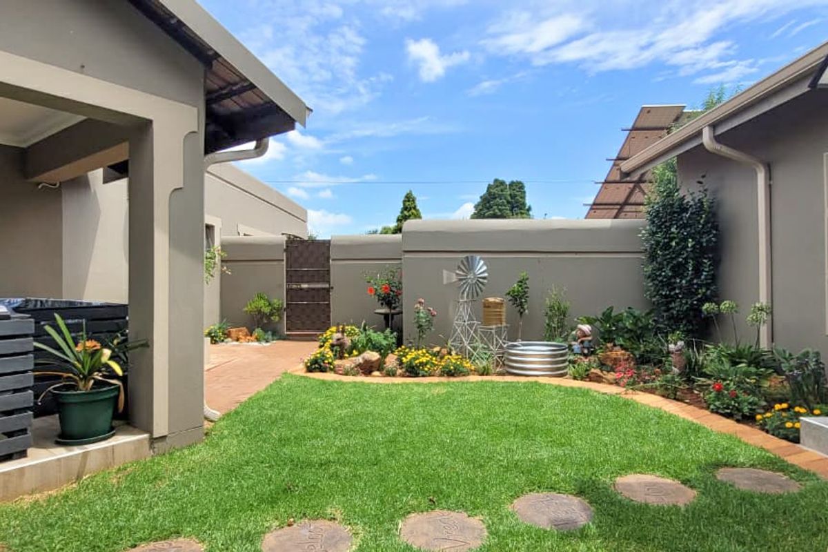 A well-maintained rear garden featuring a manicured lawn, landscaped flower beds, a covered patio area, and secure boundary walls.