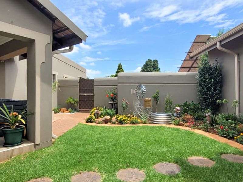 A well-maintained rear garden featuring a manicured lawn, landscaped flower beds, a covered patio area, and secure boundary walls.