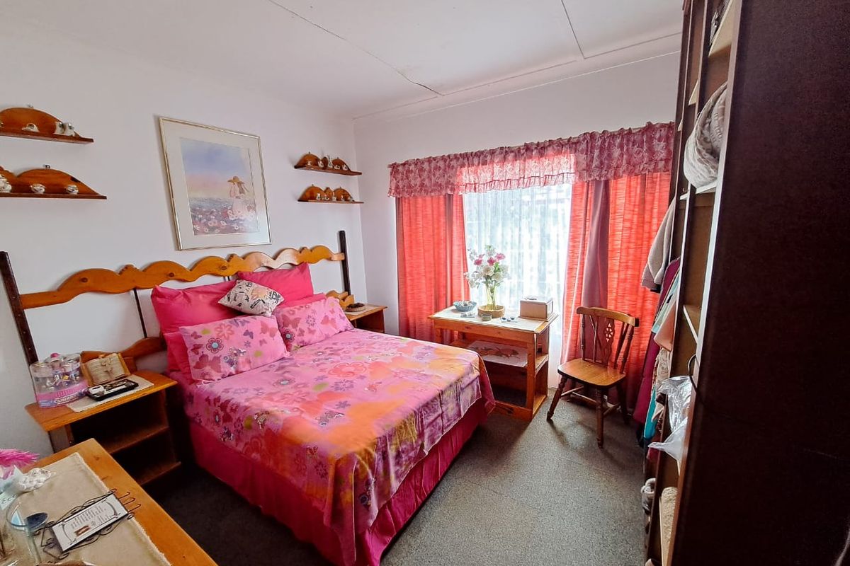A bedroom featuring carpet flooring and a window with curtain rails, showing signs of wear including a cracked ceiling.