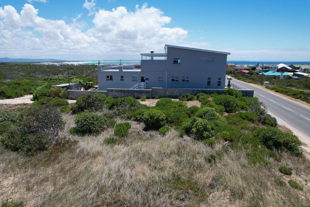 Aerial view of a modern residential property situated in a coastal landscape with a boundary wall and proximity to the road.