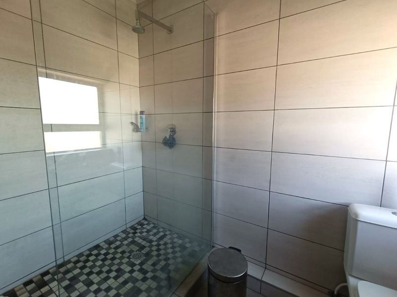 A modern bathroom featuring a glass-enclosed shower with mosaic floor tiles and neutral wall tiling, complemented by a standard toilet.