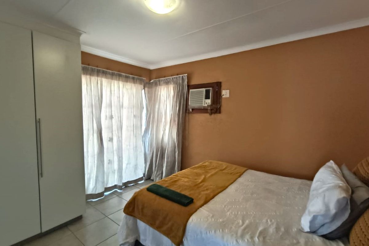 A bedroom featuring tiled flooring, a built-in wardrobe, and a window-mounted air conditioning unit.
