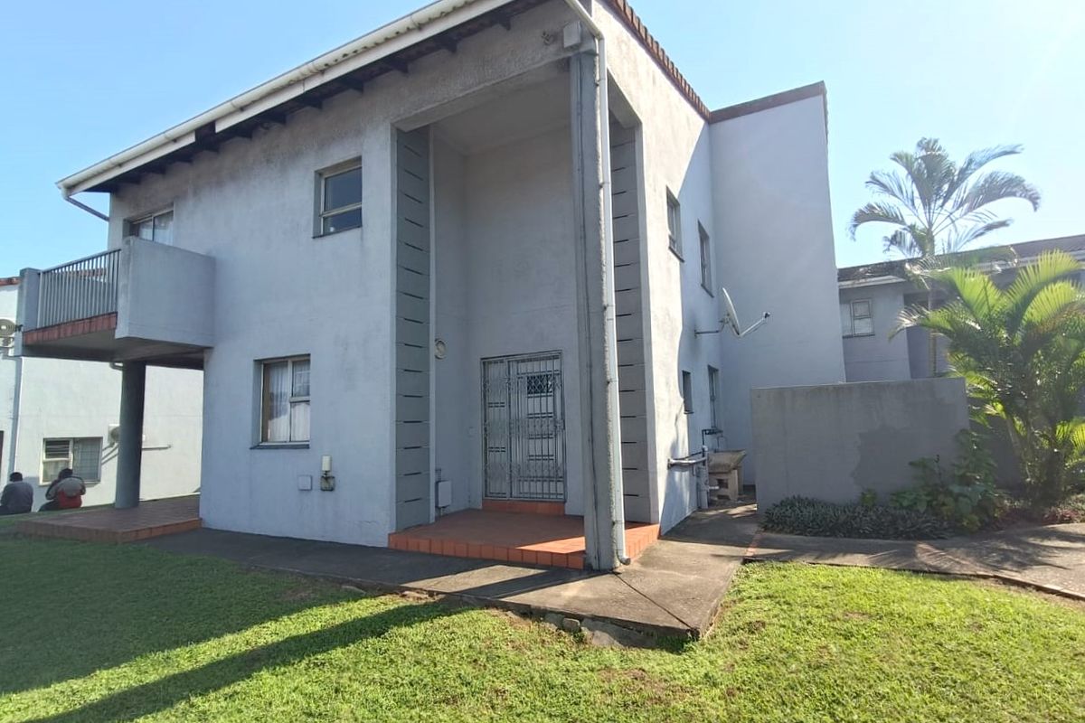 Rear view of the townhouse featuring a covered patio, balcony, and paved walkway set within a communal garden area.