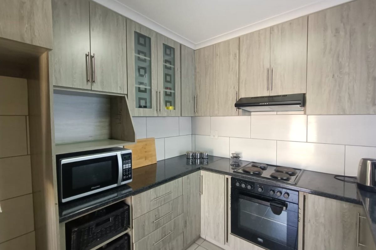 A functional kitchen featuring light wood-grain cabinetry, dark countertops, a tiled backsplash, and integrated appliances including an oven, hob, and extractor fan.