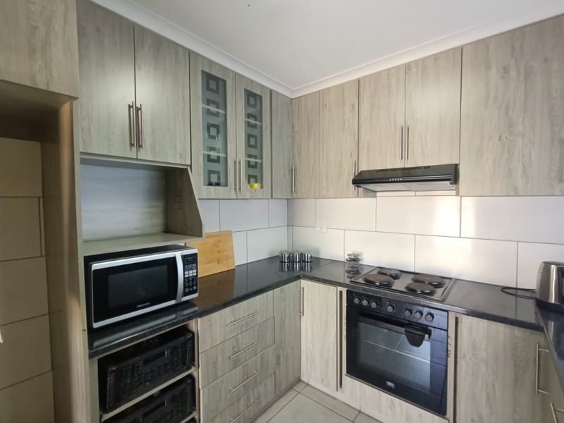 A functional kitchen featuring light wood-grain cabinetry, dark countertops, a tiled backsplash, and integrated appliances including an oven, hob, and extractor fan.