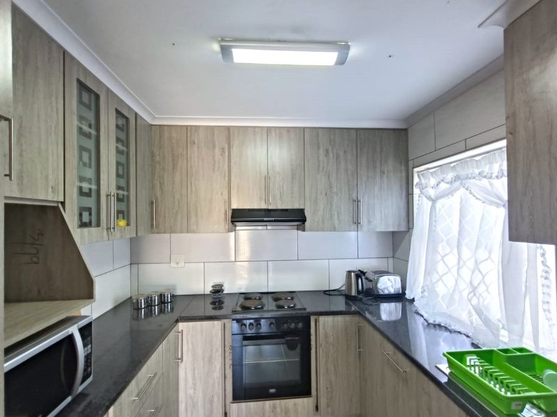A functional kitchen featuring wood-look cabinetry, dark granite countertops, a built-in oven with hob, and a tiled backsplash.