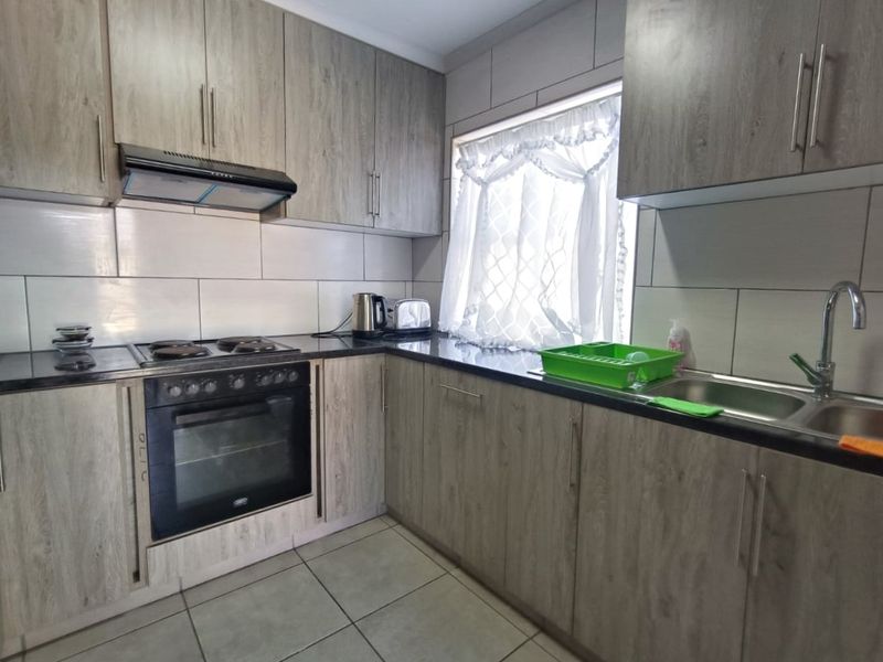 A functional kitchen featuring wood-look cabinetry, dark laminate countertops, a built-in oven with hob, extractor fan, and tiled finishes throughout.