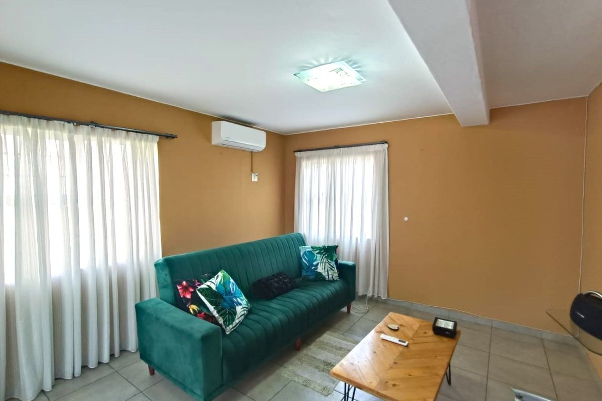 A living room featuring tiled flooring, a wall-mounted air conditioning unit, and dual windows with curtain tracks.