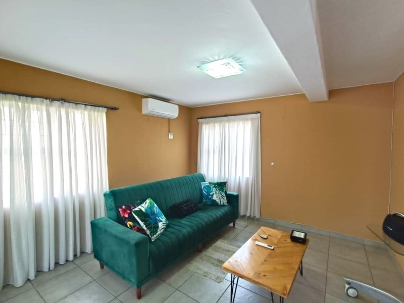A living room featuring tiled flooring, a wall-mounted air conditioning unit, and dual windows with curtain tracks.