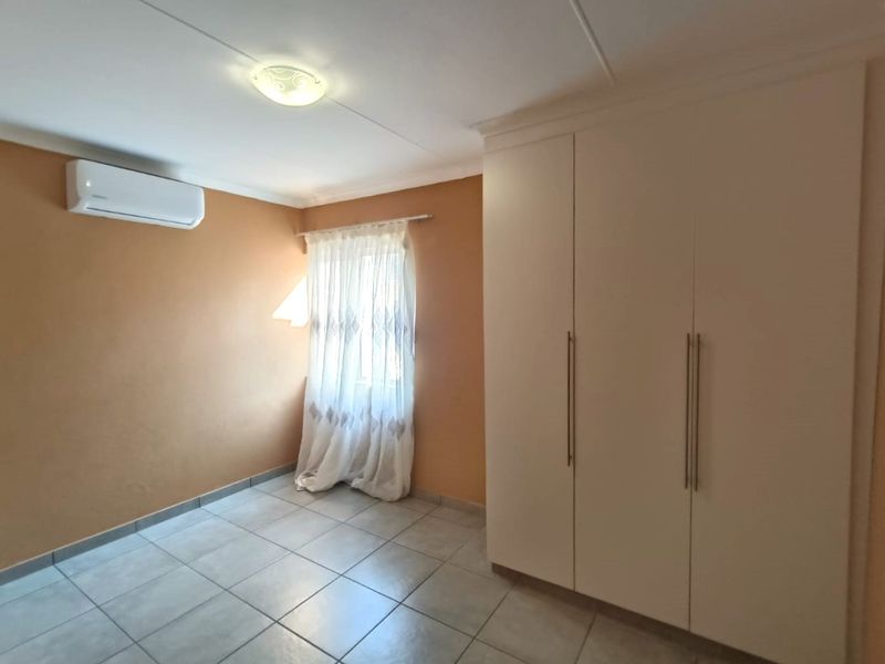 A clean, empty bedroom featuring tiled flooring, a large built-in wardrobe, and a wall-mounted split-system air conditioner.