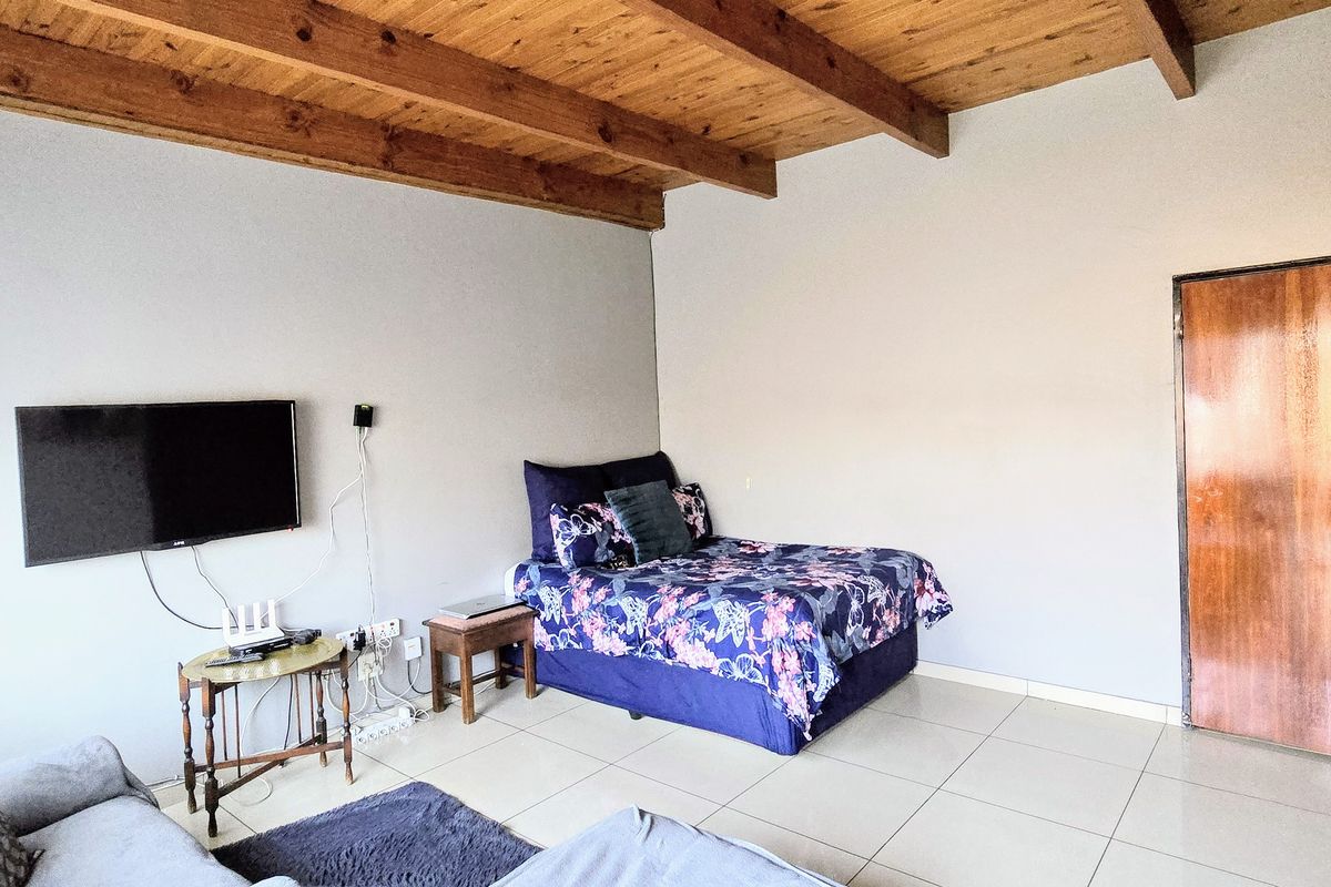 A bedroom featuring exposed timber beam ceilings, tiled flooring, and a solid wood door, offering a functional space with a rustic architectural touch.
