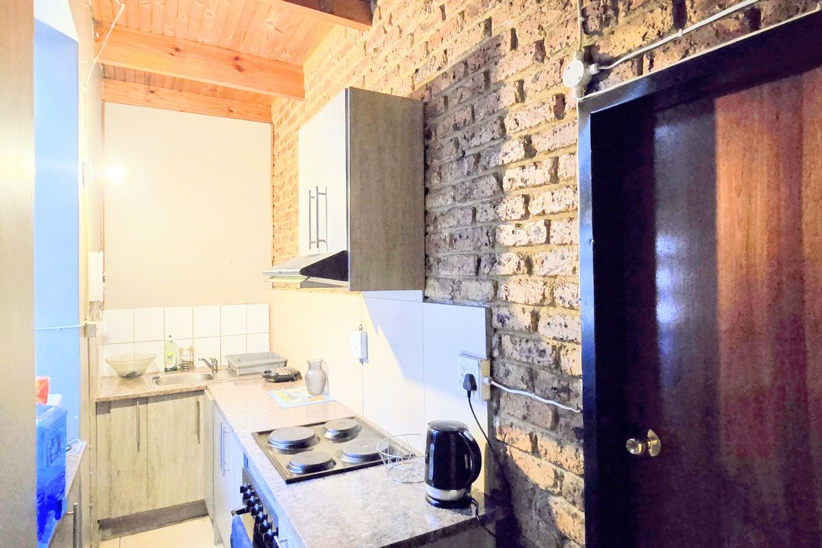 Compact kitchen featuring exposed brick walls, timber ceiling beams, built-in cabinetry, and an electric hob with an extractor fan.
