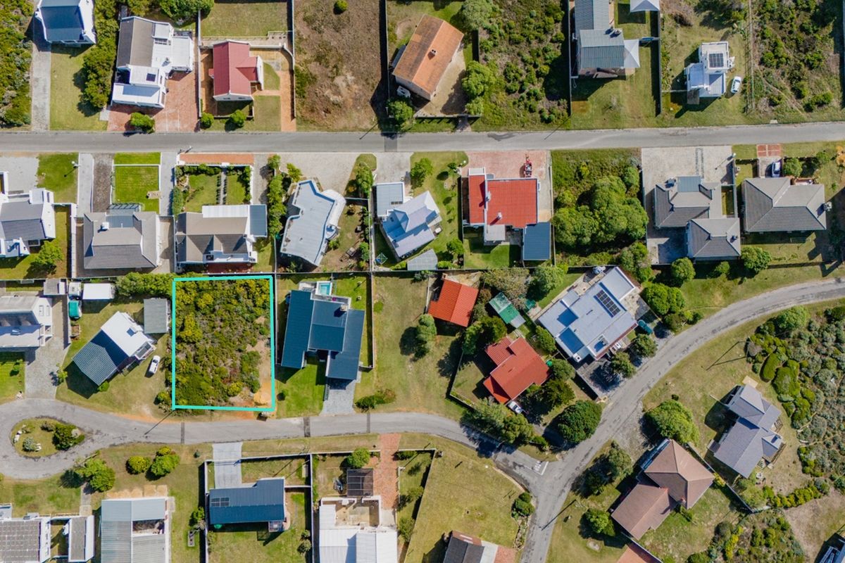 An aerial view of a vacant residential plot situated within an established coastal neighborhood, highlighting the available land and surrounding property context.