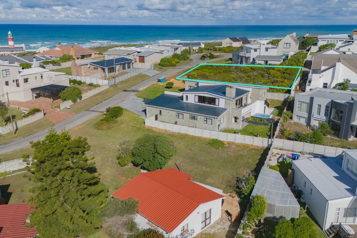 An aerial view of a vacant residential plot situated in a coastal neighborhood, highlighting its proximity to the ocean and surrounding residential properties.