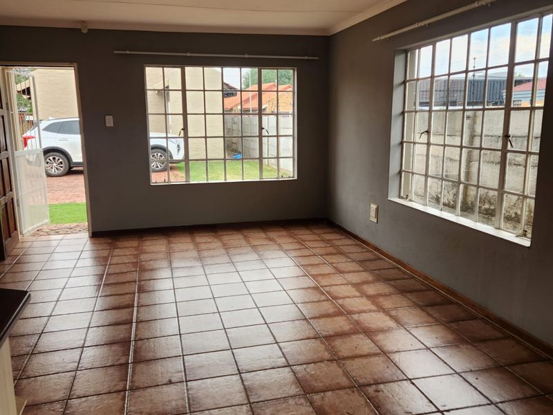 An empty living room featuring tiled flooring, large grid-pattern windows, and direct access to the exterior, offering a blank canvas for interior design.