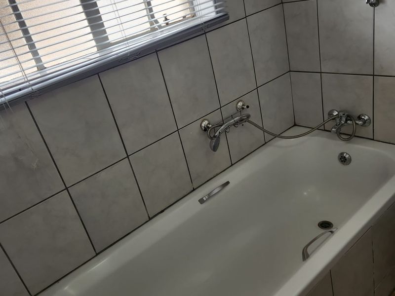 A functional bathroom featuring a built-in bathtub with wall-mounted shower fixtures and tiled wall finishes.