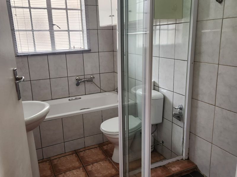 A functional bathroom featuring a bathtub, separate shower enclosure, pedestal basin, and toilet, finished with tiled walls and flooring.