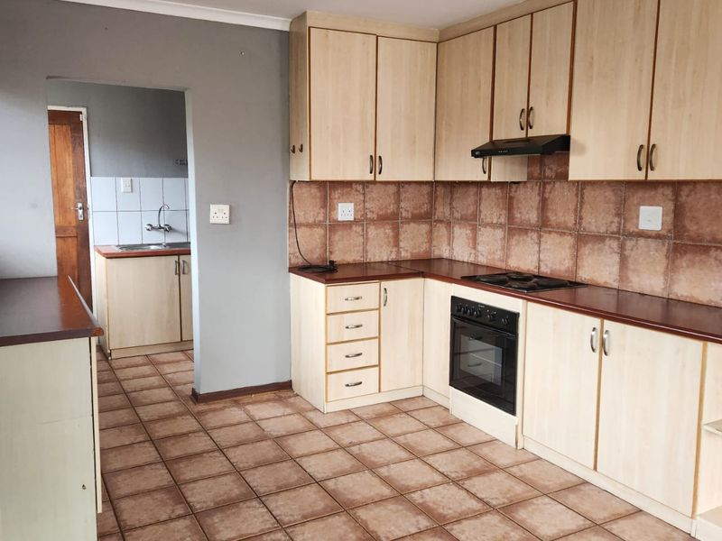 A functional kitchen featuring light wood-finish cabinetry, dark laminate countertops, and a separate scullery area with additional sink and storage space.