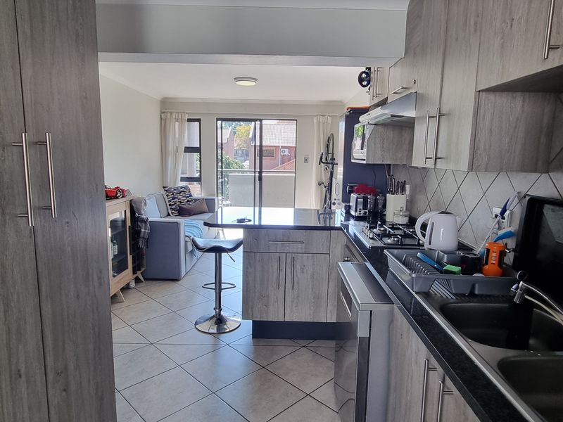 Open-plan kitchen and living area featuring modern wood-look cabinetry, granite countertops, gas hob, and direct access to a balcony through sliding glass doors.