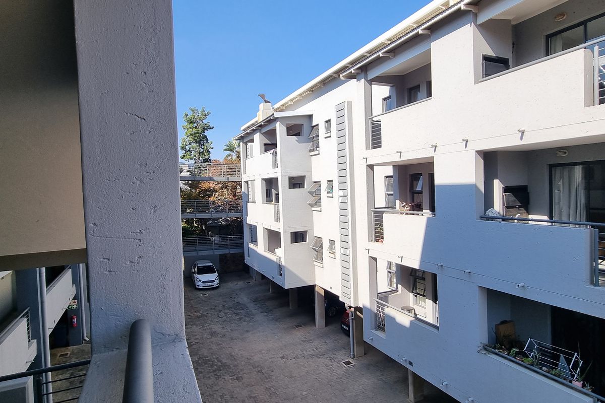 View of the apartment complex rear courtyard, featuring paved parking area, multiple balconies with metal railings, and external building access.
