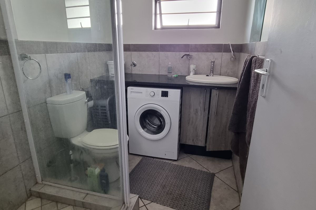 Functional bathroom featuring a shower enclosure, vanity with basin, and integrated laundry space with washing machine connection.