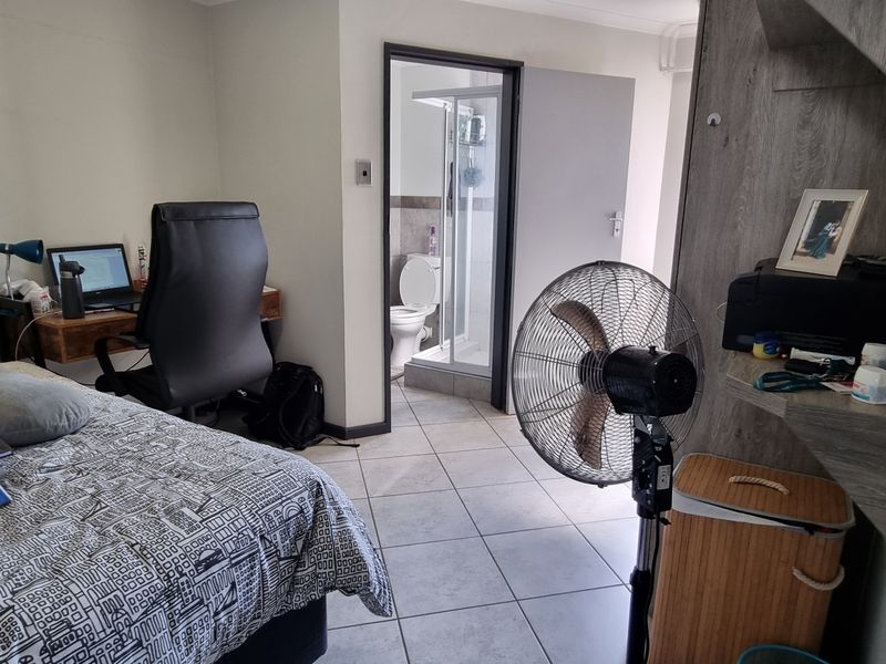 A bedroom featuring tiled flooring and a built-in shelving unit, with direct access to an en-suite bathroom.