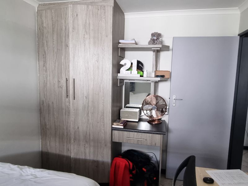 A bedroom featuring a built-in wood-grain wardrobe and integrated vanity unit with shelving, providing functional storage and a dedicated dressing area.