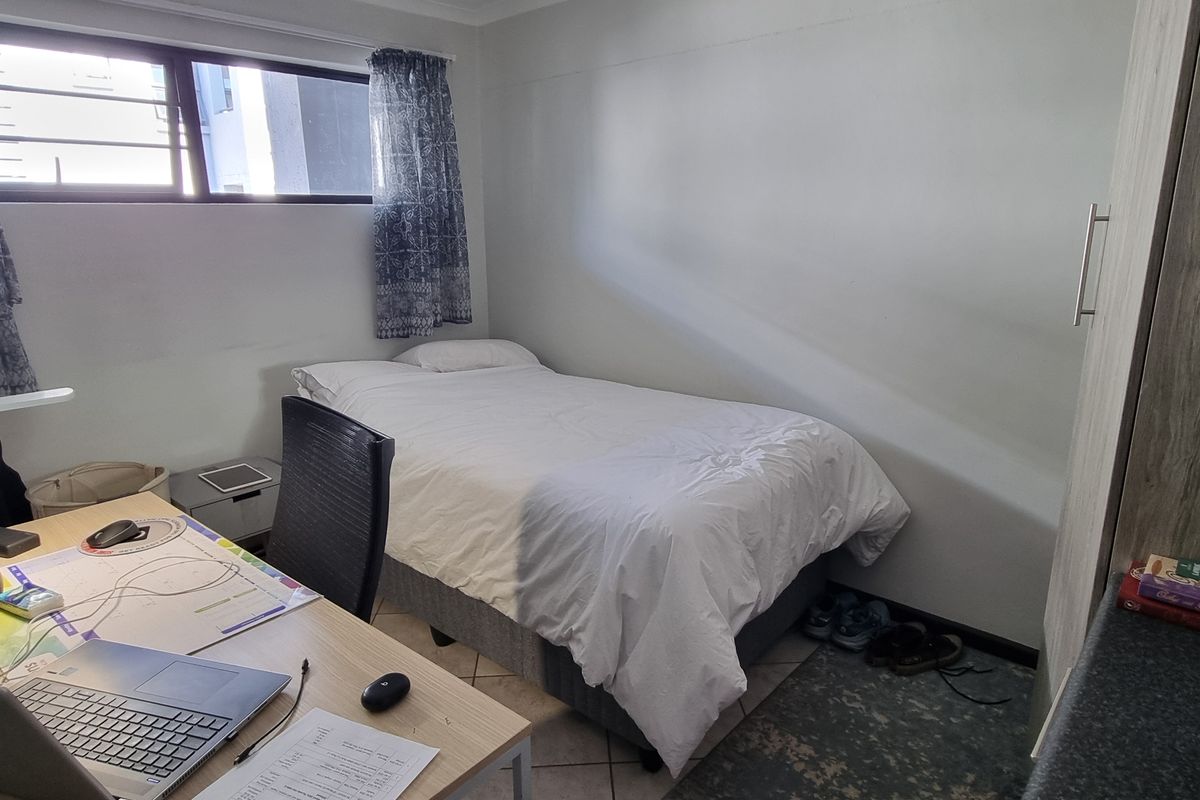 A compact bedroom featuring tiled flooring, a built-in cupboard, and a window providing natural light.