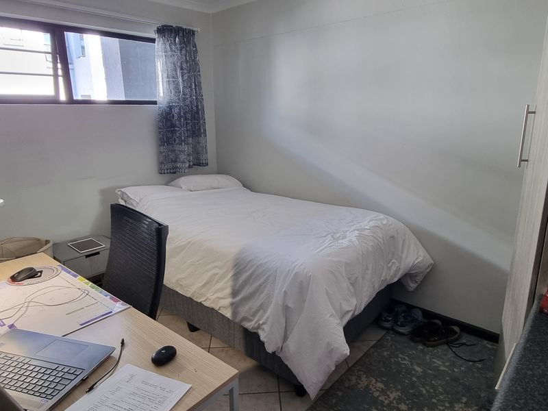 A compact bedroom featuring tiled flooring, a built-in cupboard, and a window providing natural light.