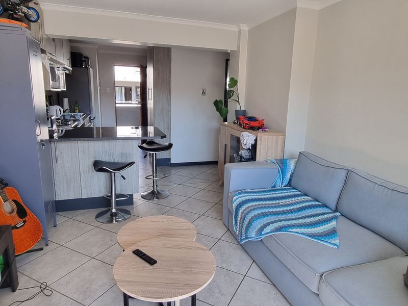 Open-plan living area featuring tiled flooring and a functional kitchen with a breakfast bar, creating a cohesive and practical living space.
