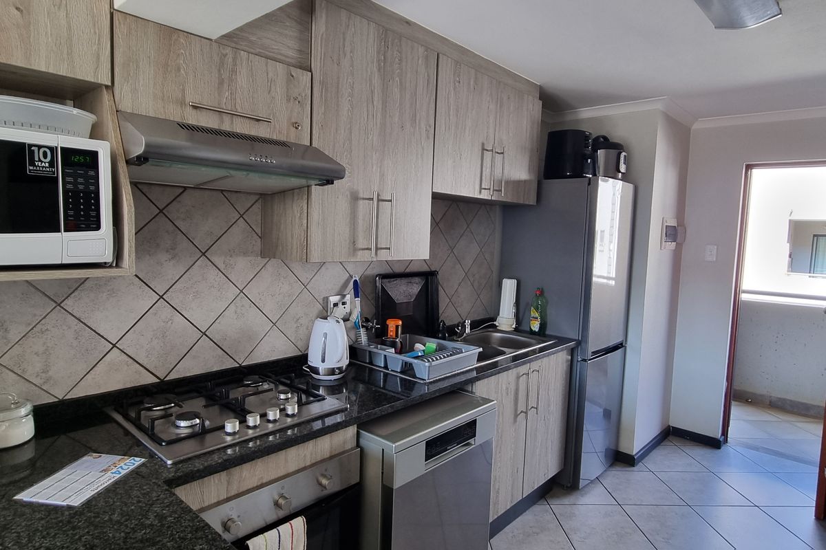Modern kitchen featuring wood-grain cabinetry, granite countertops, gas hob, extractor fan, and tiled finishes, with direct access to an outdoor balcony area.