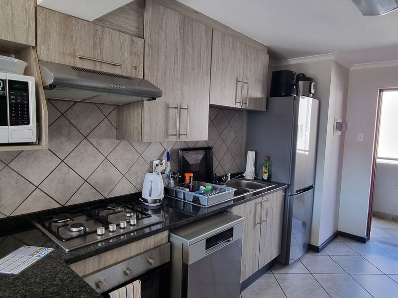 Modern kitchen featuring wood-grain cabinetry, granite countertops, gas hob, extractor fan, and tiled finishes, with direct access to an outdoor balcony area.