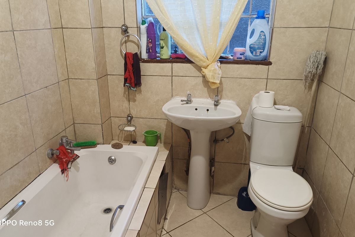 A compact bathroom featuring a pedestal basin, bathtub, and toilet with full-height wall tiling and tiled flooring.