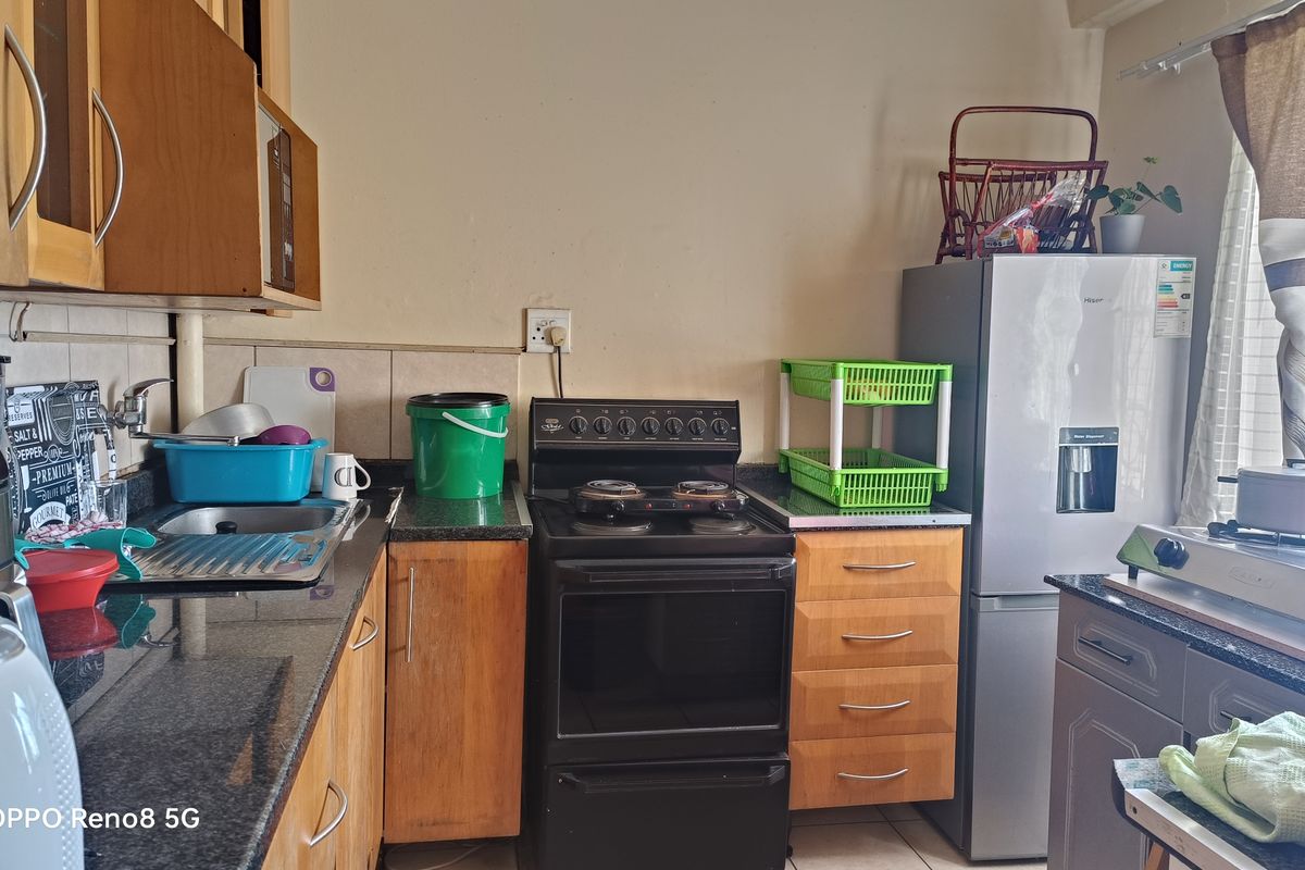 A functional kitchen featuring granite countertops, wooden cabinetry, a stainless steel sink, and a freestanding stove with a tiled backsplash.