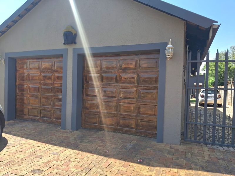 A double garage with wooden panel doors, paved driveway access, and integrated security gate.