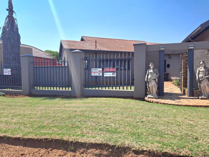 Front exterior view of the property featuring a paved entrance, metal perimeter fencing, and a well-maintained lawn.