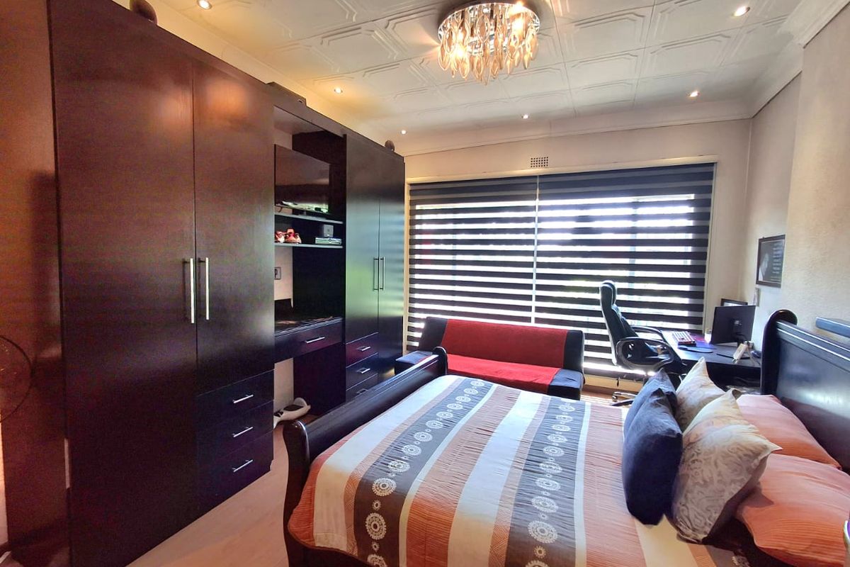 A well-maintained bedroom featuring extensive built-in cabinetry, decorative ceiling detailing, recessed lighting, and large windows fitted with modern roller blinds.