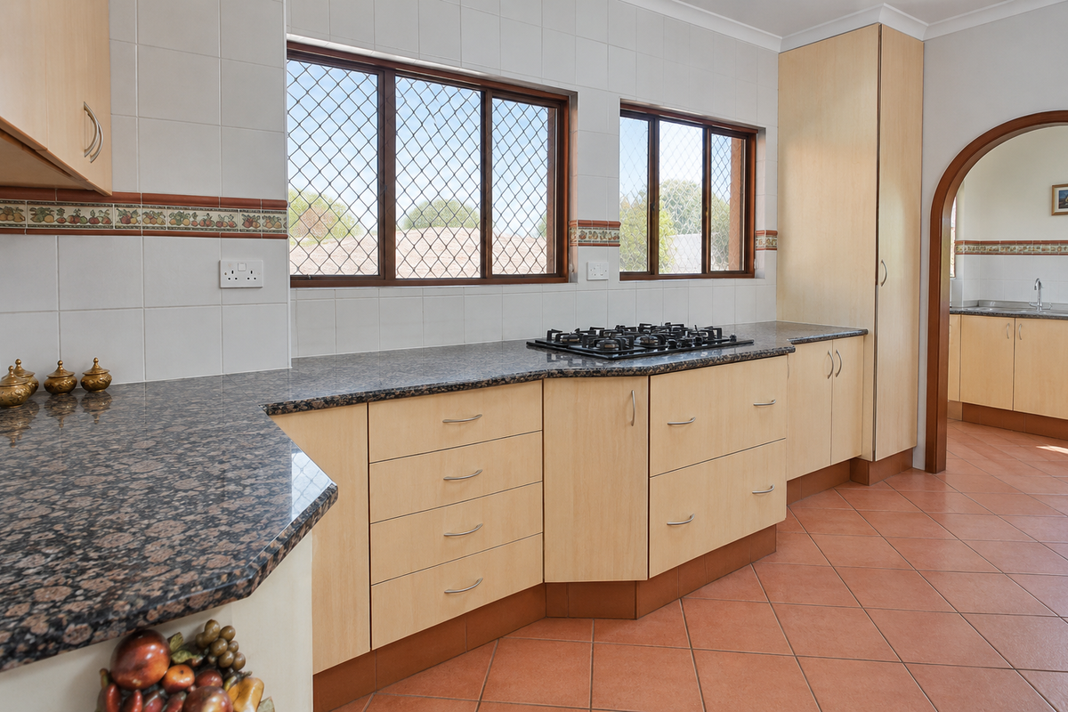 A functional kitchen featuring granite countertops, a gas hob, light wood cabinetry, and tiled flooring, with an arched doorway leading to an adjacent space.